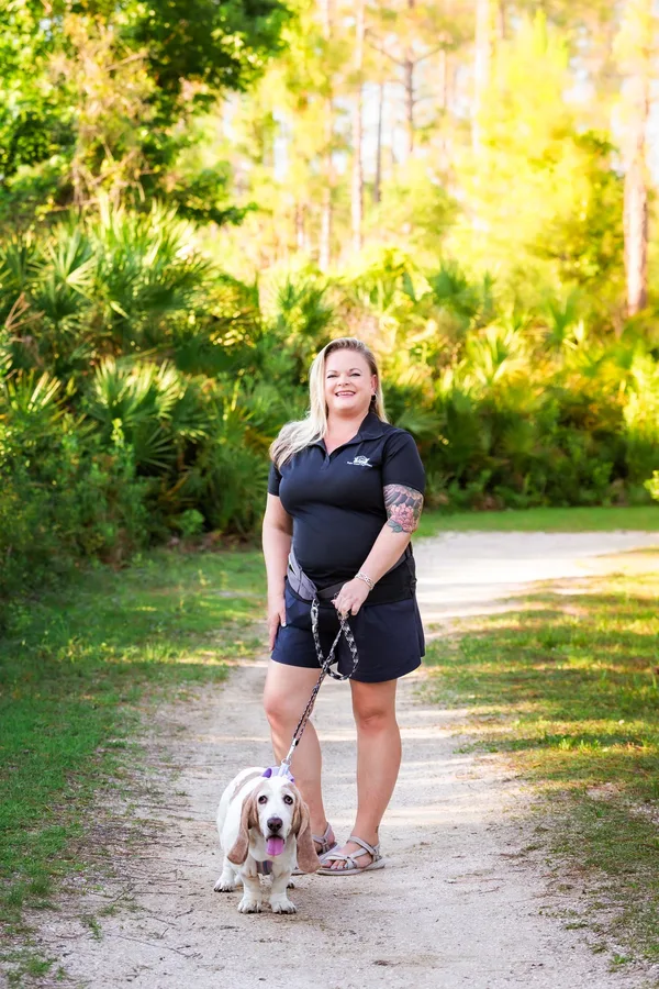 Kelly, owner of Palm Coast Pet Sitters, on a sandy trail with a basset hound on a leash.
